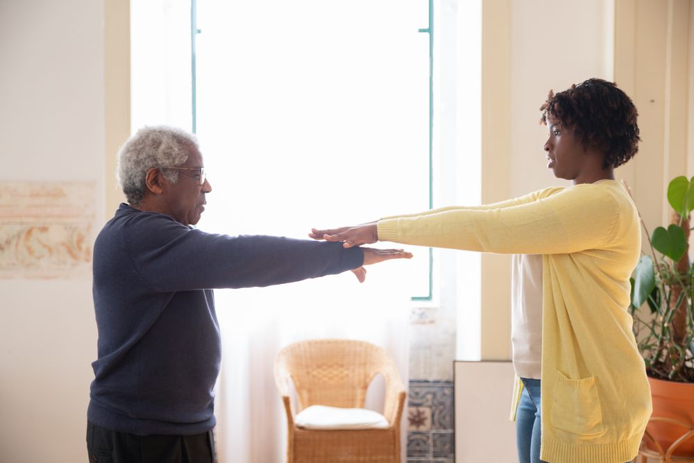 A healthcare caregiver helping an older adult exercise at home