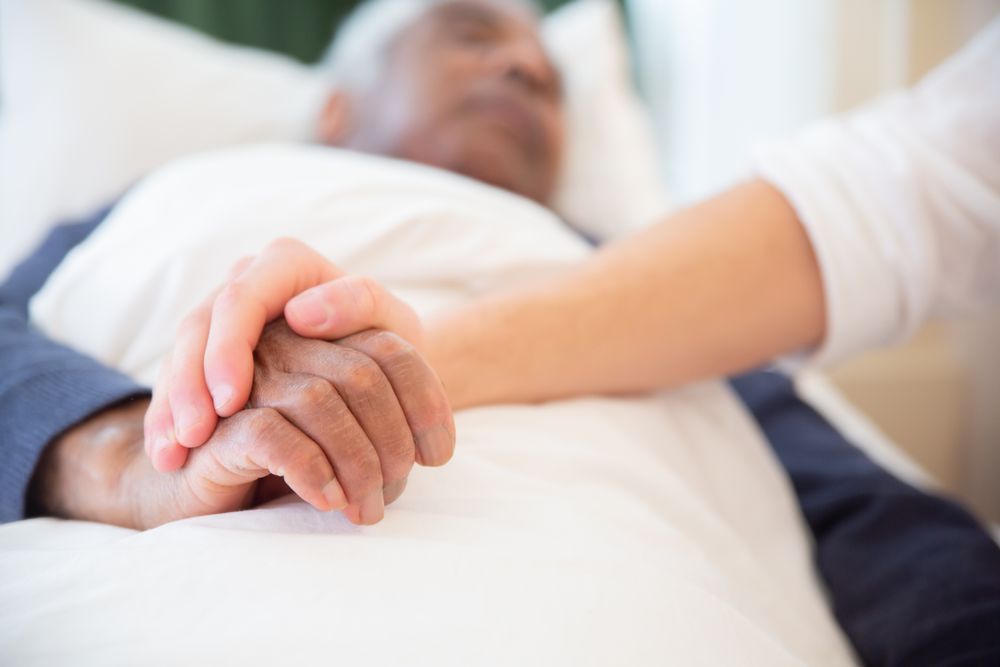 A caregiver gently holding an elderly patient’s hand